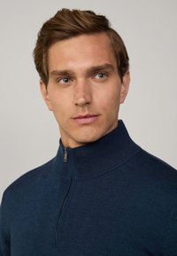 Marineblaues Reißverschluss-Sweatshirt aus strukturiertem Strickstoff, hoher Kragen, Viertel-Reißverschluss-Detail an der Vorderseite, minimalistisches Design ohne Muster oder Akzente.