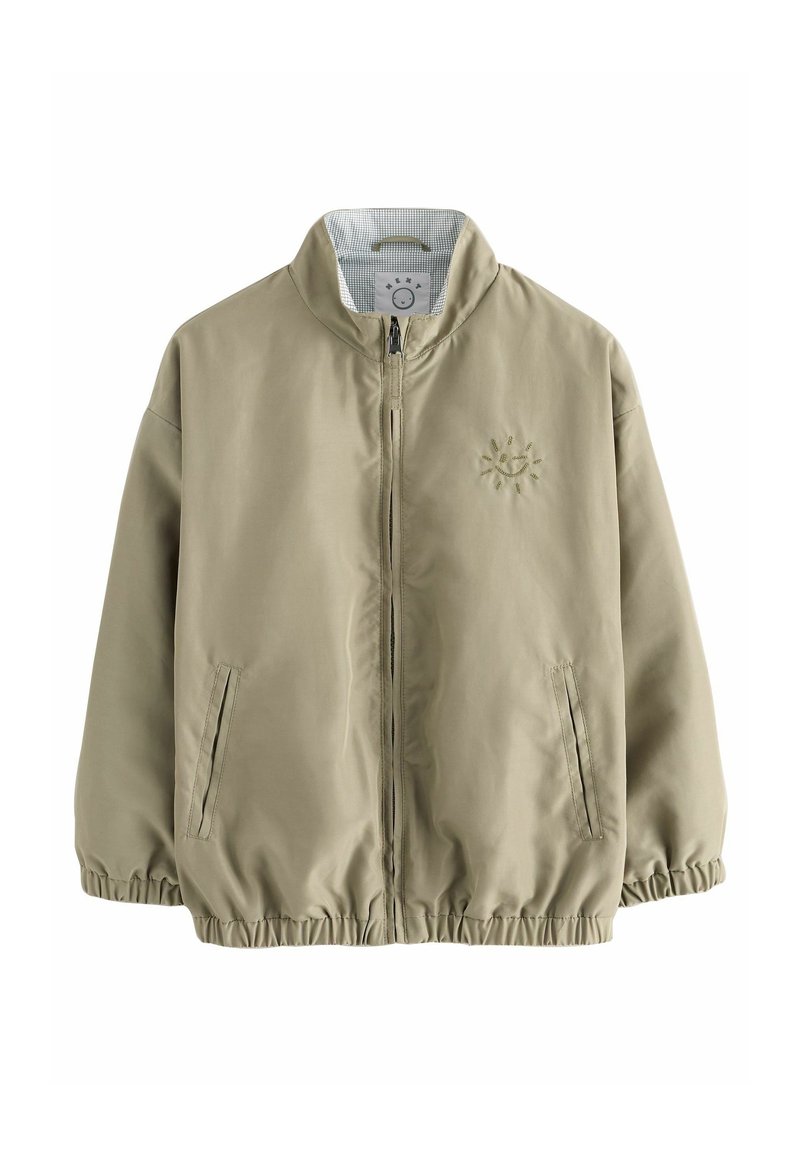 Veste marron clair zippée avec poignets et ourlet élastiques, deux poches avant et un petit soleil brodé sur la poitrine gauche.