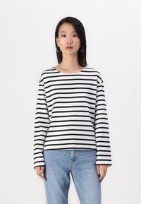 Svart og hvit stripete langermet skjorte med rund hals, laget av et lett stoff. Kombinert med lyseblå denimjeans.