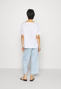 Valkoinen pellavapaita lyhyillä hihoilla ja selässä avaimenrei'ellä, yhdistettynä vaaleansinihin leveälahkeisiin housuihin ja mustiin tasapohjaisiin sandaaleihin.