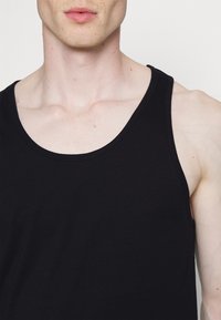 Débardeur en coton noir avec un col rond et de larges bretelles. Le tissu semble lisse avec des détails de couture minimes.