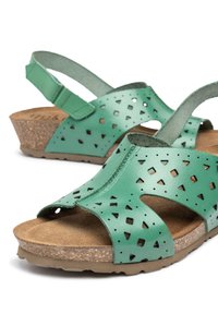 Sandalias de cuero verde con patrones recortados, un diseño de punta abierta, una plantilla de corcho y una suela baja en cuña para mayor comodidad.
