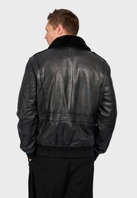 Černá kožená bomber bunda s límcem z ovčí kožešiny, žebrovanými manžetami a pasem. Hladká textura s viditelnými švy na zadní straně.