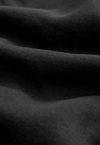 Musta kangas, jossa on sileä tekstuuri, jossa on hienovaraisia vaakasuuntaisia neulekuvioita ja pehmeää laskostumista. Ei näkyviä yksityiskohtia tai koristeita.