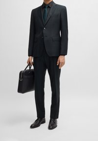 Completo verde scuro motivo, con giacca monopetto e pantaloni abbinati. Include scarpe eleganti nere e una borsa in pelle nera.