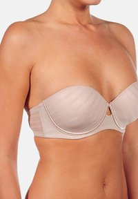 Sujetador sin tirantes de color beige con textura acanalada, soporte con aros y un pequeño detalle de ojal en el centro, acabado con un ribete en tono dorado rosa.