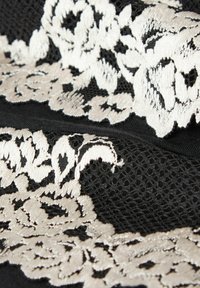 Zwart stof met intrigerende beige bloemenkantdetails, voorzien van een textuurmesh element en elegante geborduurde accenten.