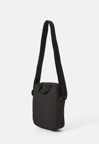 Bolso bandolera negro de forma rectangular, hecho de tejido duradero. Cuenta con una correa ajustable y un asa en la parte superior para mayor comodidad.