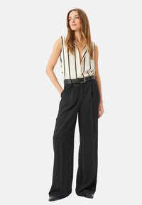 Blusa sin mangas a rayas en crema y negro, combinada con pantalones negros de cintura alta. Presenta un cinturón y pliegues para un diseño estructurado.
