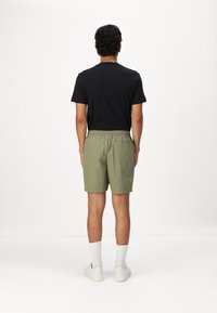 Camiseta negra de manga corta y pantalones cortos verde oliva con una cinturilla elástica, mostrados desde la parte de atrás, llevados con calcetas blancas y zapatillas.