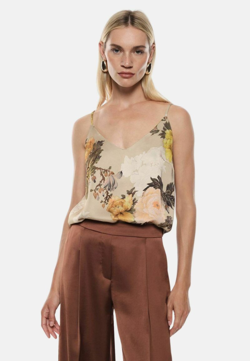 Camicetta in satin floreale beige con motivi gialli, bianchi e verdi; presenta spalline sottili e scollatura a V. Abbinata a pantaloni marroni.