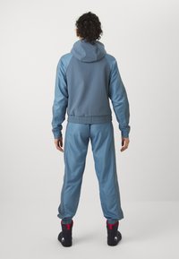 Fato de treino azul com um casaco com capuz, punhos e cintura elásticos, combinado com calças coordenadas e detalhes contrastantes.