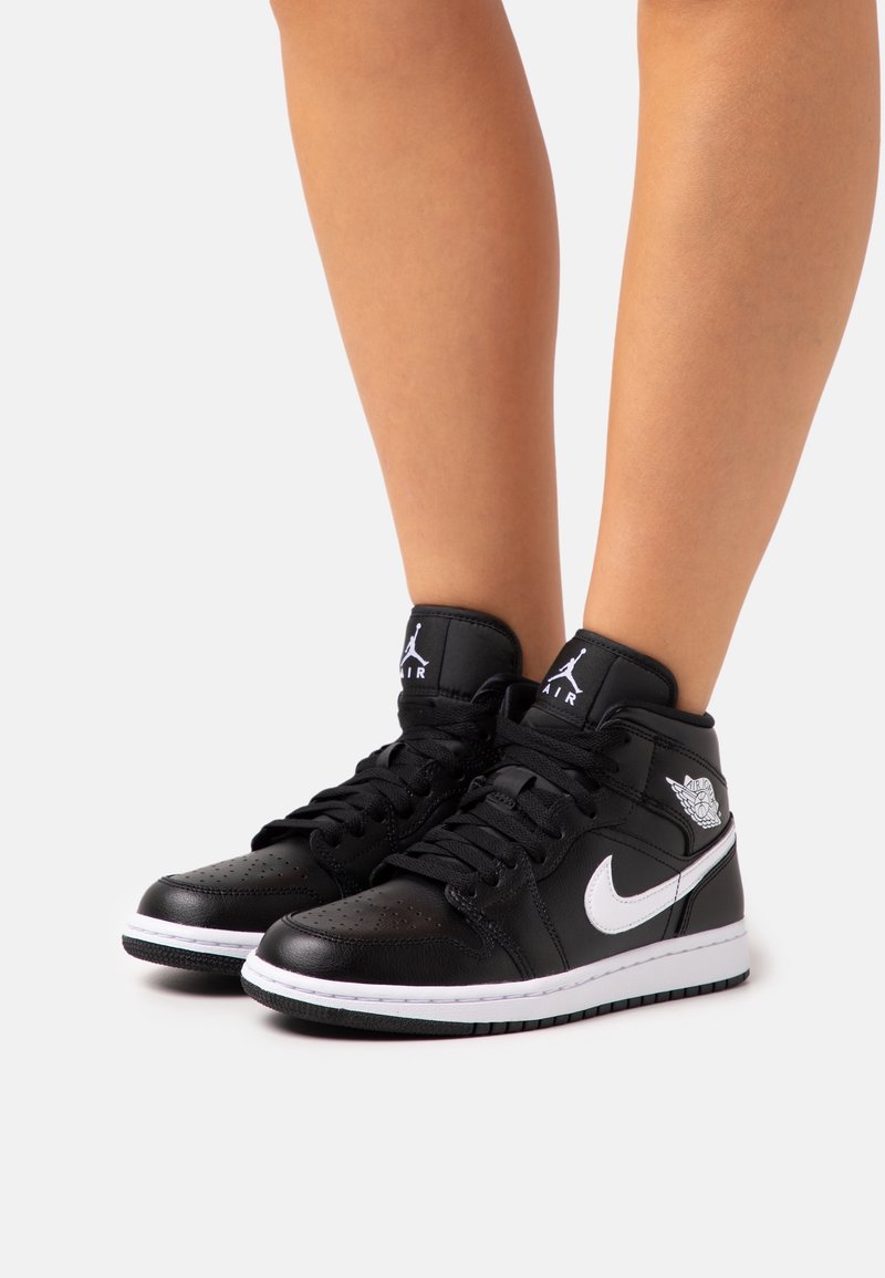 Sneaker alte in pelle nera con accenti bianchi, punta forata e logo Air Jordan sulla caviglia e sul lato. Suola in gomma.