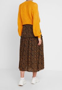 Yellow knitted sweater with a chevron pattern, paired with a black floral skirt featuring orange and blue accents, finished with white sneakers.