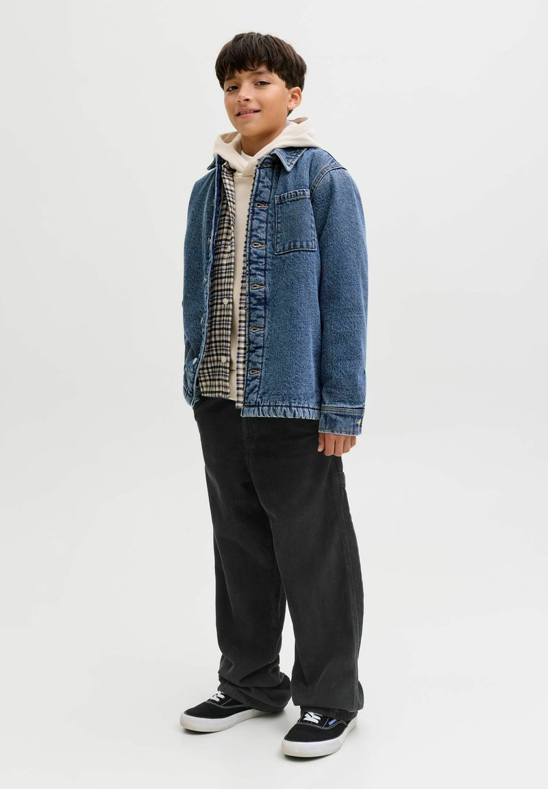 Jeans jakna s plavim pranjem, složena preko košulje od kariranog flanela i bijelog duksera. Crne kordura pantalone i crne patike upotpunjuju izgled.
