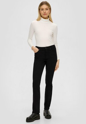 Schwarze Slim-Fit-Jeans mit glatter Textur, ausgestattet mit frontalen Taschen. Kombiniert mit einem enganliegenden weißen Langarm-Poloshirt.