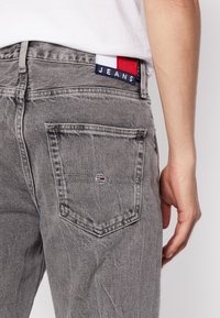 Vaqueros de mezclilla gris con una textura descolorida, que cuentan con un bolsillo trasero y una etiqueta que muestra colores azul, blanco y rojo con el texto "JEANS".