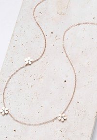 Collana con catena in oro rosa che presenta tre pendenti a forma di fiore con piccole gemme chiare al centro, posizionata su uno sfondo neutro.