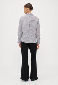 Striped button-down shirt in black and white with a collar, long sleeves, and a relaxed fit. Paired with black flared pants.