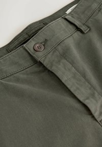 Close-up of olive green pants waistband with button closure and textured fabric.
