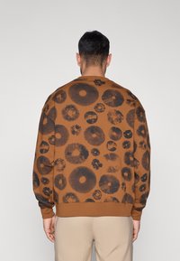 Καφέ φούτερ με μαύρο ανθικό σχέδιο, με στρογγυλά σχήματα και υφές. Διαθέτει ριμπ λαιμόκοψη και μανσέτες, σχεδιασμένο για άνετη εφαρμογή.