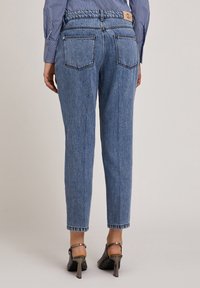 Jeans de denim azul deslavado con un corte recto, cinco bolsillos y una etiqueta de cuero en la cintura; combinados con tacones negros y puños doblados.