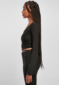 Černý žebrovaný dlouhý rukáv crop top s výstřihem do V, se zkrouceným předním dílem a přiléhavými rukávy. V kombinaci s odpovídajícími legínami s vysokým pasem.