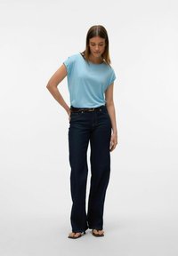 Top azzurro chiaro a maniche corte abbinato a jeans a zampa d'elefante blu scuro e sandali neri, caratterizzato da una texture liscia e una vestibilità classica.