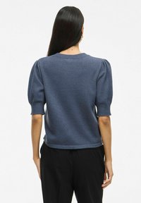 Pull en tricot bleu marine à manches courtes avec épaules bouffantes, col rond et ourlet côtelé, arborant une coupe légèrement ample et une texture lisse.
