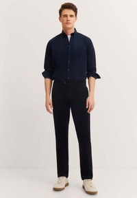 Navy button-up shirt, slim-fit black pants, and white sneakers. Smooth fabric, long sleeves, and a front pocket detail on the shirt.