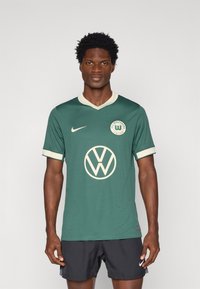 Roheline Nike jakk kreemjate aktsentidega ja Volkswageni logo, millel on V-kaelus ja lühikesed varrukad. Materjal tundub hingav.