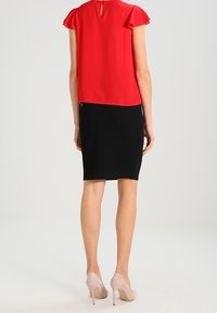 Rød kortærmet bluse med en nøglehulsryg, parret med et tætsiddende sort nederdel og nude højhælede sko. Glat stof, enkelt design.