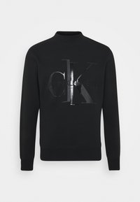 Felpa nera a maniche lunghe con polsini e orlo a costine, con un logo lucido "CK" e "Calvin Klein Jeans" al centro davanti.