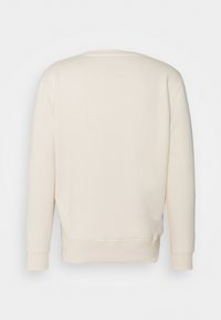 Felpa color crema con colletto rotondo, polsini e orlo a costine. Design semplice con un piccolo dettaglio a etichetta quadrata sulla parte superiore della schiena.