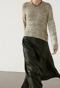 Pull en tricot marron clair avec un large col et des manches longues, associé à une jupe en satin noir fluide. Design simple et texturé.