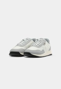 Sneaker con una parte superiore grigio chiaro e bianca, con una finitura texturizzata, lacci piatti e una suola in gomma nera con un sottopiede a contrasto.