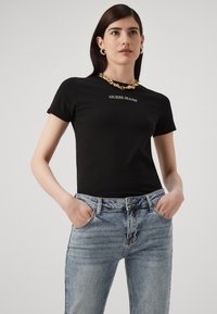 Fekete pamut póló rövid ujjú, "GUESS JEANS" logóval. Világoskék farmernadrággal párosítva, amely klasszikus fazonnal és elülső zsebekkel rendelkezik.