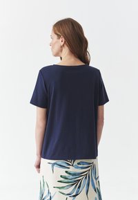 Camiseta de algodón azul marino de mangas cortas, de corte recto y con escote redondo, combinada con una falda que presenta patrones de hojas verdes y azules.