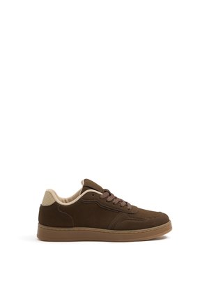 Zapatilla baja marrón con cuello acolchado beige, cordones marrones y suela de goma marrón claro, mostrada de lado sobre fondo blanco.