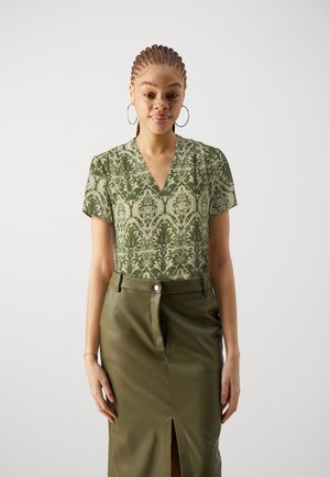 Olive green blouse with a damask pattern, short sleeves, and a V-neck, paired with a high-waisted, fitted olive green leather skirt featuring a front slit.