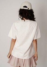 Bawełniany t-shirt w jasnym kremowym kolorze, o luźnym kroju, z krótkimi rękawami i zaokrąglonym dekoltem, zestawiony z jasnoróżową spódnicą z falbanami.