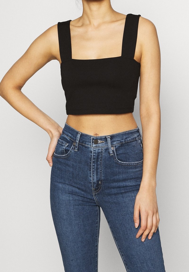 Crop top noir avec décolleté carré et bretelles larges, associé à un jean en denim bleu taille haute. Design simple, texture lisse.