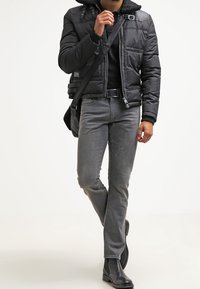 Musta puffatakki, jossa on turkilla vuorattu kaulus, harmaat slim-fit farkut ja mustat nilkkurit. Henkilöllä on mukanaan musta olkalaukku.