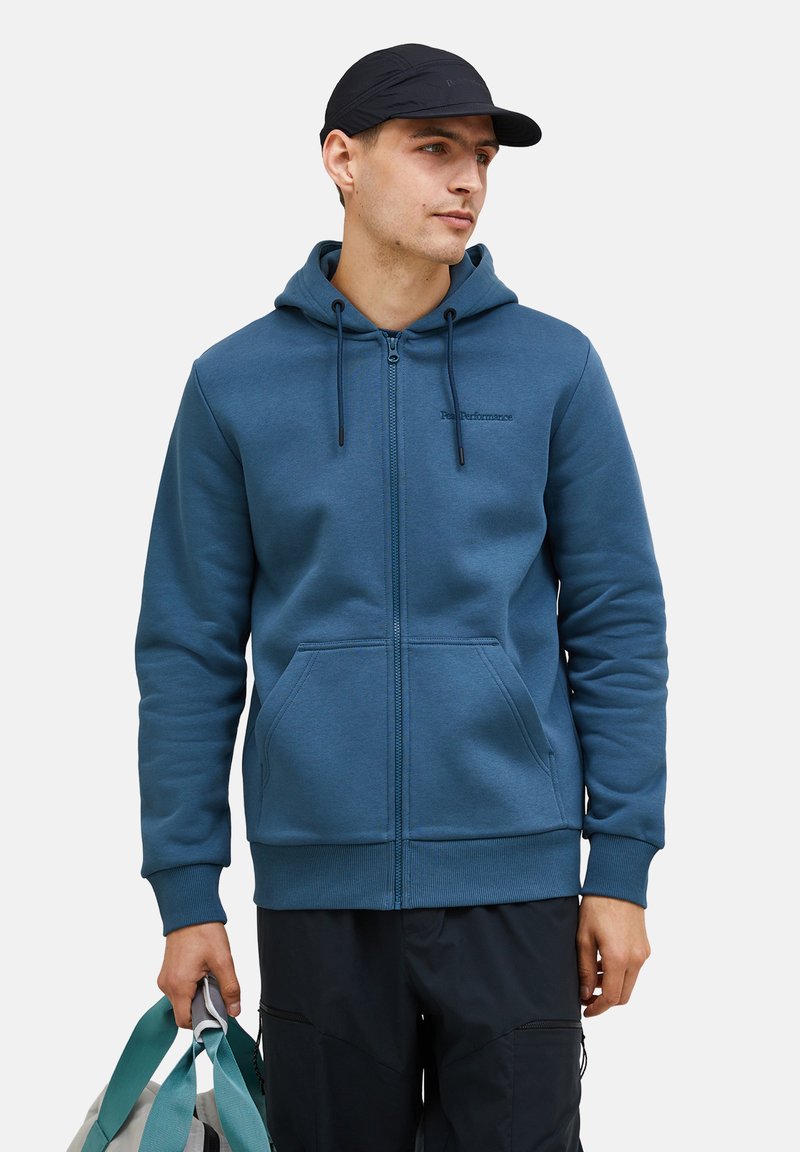 Svijetloplavi zip-up dukserica s kengurubažnom džepom, kapuljačom na šnuru i rebrastim manžetama. Logo otisnut na lijevoj strani prsnog koša. Tkanina izgleda glatko.