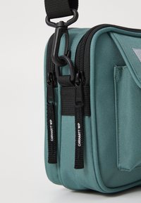 Geantă tip crossbody din nailon teal, cu fermoare duble, elemente de hardanger negre și curea ajustabilă. Prezintă un material texturat și fermoare cu logo.