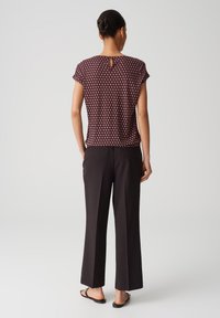 Kortærmet bordeaux top med et geometrisk mønster, der har en nøglehul-åbning bagpå, sat sammen med sorte, vide bukser og sorte sandaler.