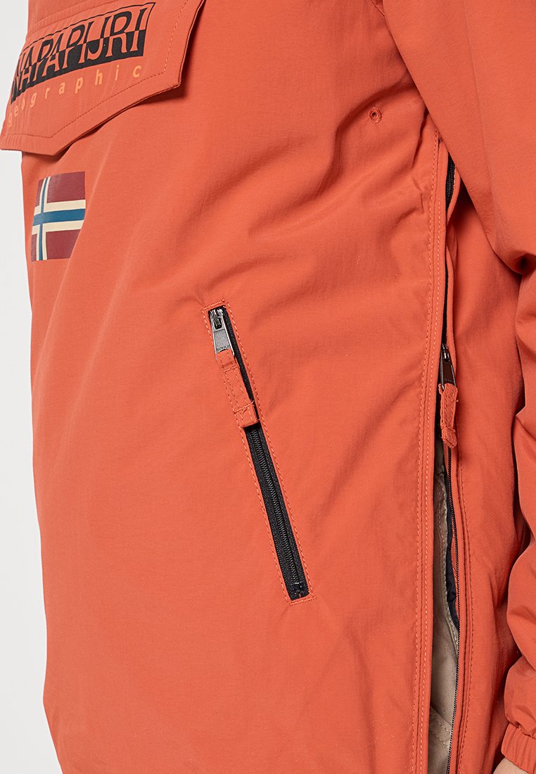 Giacca esterna arancione con tasca con zip, patch con logo ed emblema della bandiera. Tessuto liscio e vestibilità rilassata. Dettaglio di cuciture visibile.