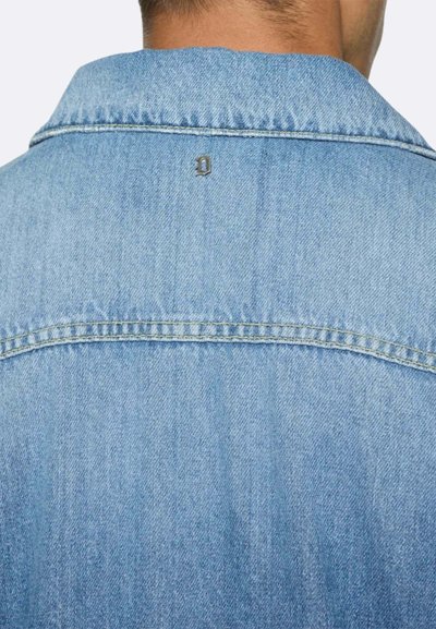 Giacca di jeans di colore azzurro chiaro, con colletto classico e un sottile particolare in metallo sul retro. Dettagli di cucitura visibili.