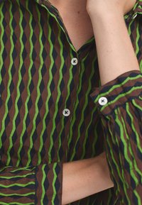 Bruine shirt met groen en marineblauwe ruitpatroon, met een knoopsluiting aan de voorkant, omgeslagen mouwen en een gladde textuur.