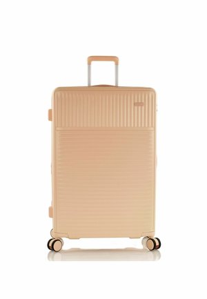 Maleta rígida en un tono melocotón claro con textura acanalada vertical. Cuenta con un mango telescópico y cuatro ruedas negras y doradas para facilitar el movimiento.